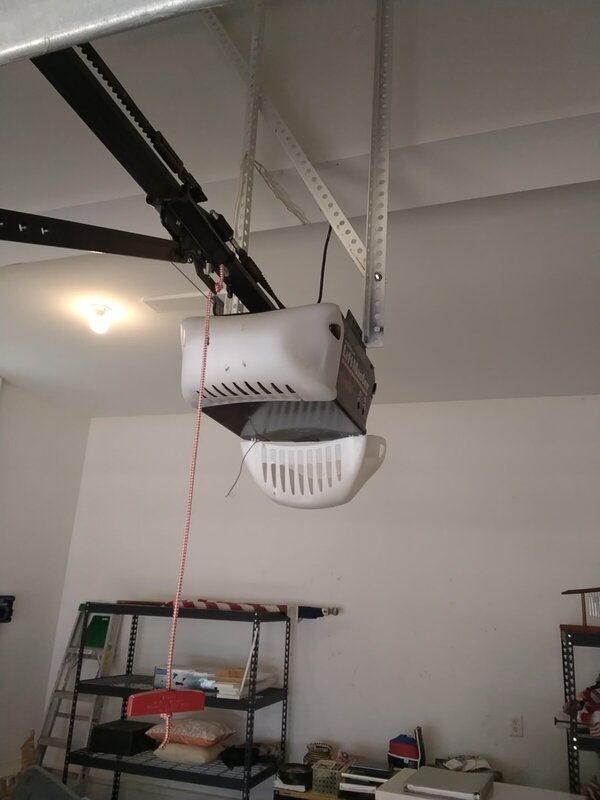 Old ceiling-mounted chain-drive garage door opener with a red emergency-release cord, before removal, in a Ford's Colony, Williamsburg 23185 garage