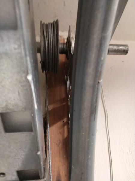 Garage door cable diagram in real life: lift cable on the cable drum at the end of the torsion shaft, dropping between the vertical track and the wood jamb