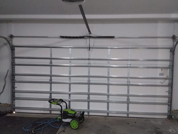 Garage door out of balance in Suffolk VA: the wide steel door closed, torsion springs on the shaft above it and the LiftMaster opener rail, before the adjustment